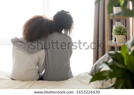 Loving african american single mother sister embrace teen daughter sit on bed looking at window, parent mom hug support protect teenage girl, family trust hope talk understanding concept, rear view Royalty-Free Stock Photo #1653226630