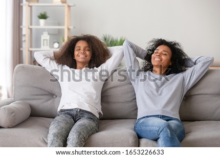 Calm lazy african family mom and daughter stretch relax on comfortable sofa at home, happy healthy black mother with teen girl rest together breathing fresh air enjoy no stress day feel satisfaction Royalty-Free Stock Photo #1653226633