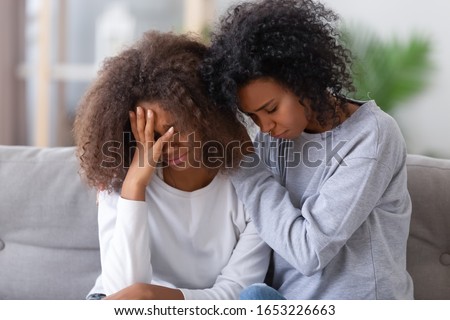 Upset african american mom sister hugging sad child teen girl consoling supporting or asking for forgiveness after fight, black mother hugging comforting depressed teenage daughter sitting on sofa Royalty-Free Stock Photo #1653226663