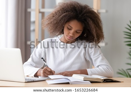 Focused african american school girl studying with books laptop preparing for test exam writing essay doing homework at home, teenage student learning assignment making notes, teen education concept Royalty-Free Stock Photo #1653226684