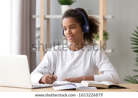 African teen girl wearing headphones study with internet chat skype teacher prepare for exam, black girl school student learning online, watch webinar make notes looking at laptop, distance education Royalty-Free Stock Photo #1653226879