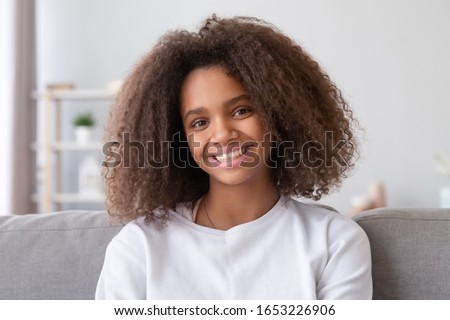Head shot of smiling mixed race teen girl looking at camera at home, happy african american teenager posing indoors, teenage high school student vlogger blogger influencer igeneration child portrait