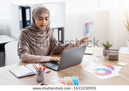 Modern Profession. Portrait of busy arabic female graphic designer working on new project with color swatches and laptop in office, free space