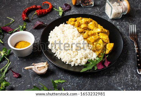 Rice with chicken in curry sauce on plate on black stone background Royalty-Free Stock Photo #1653232981