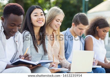 Intelligent international students preparing for final exams at public park, using laptop and notebooks