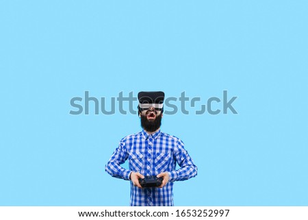 surprised bearded man in VR (virtual reality glasses) with remote control in hand controls the drone, image on blue background