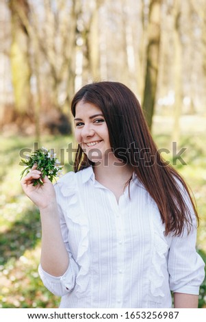 girl in the park with spring flowers, white anemones. Brunette in white shirt with flowers in hands