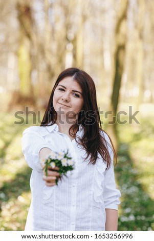 girl in the park with spring flowers, white anemones. Brunette in white shirt with flowers in hands