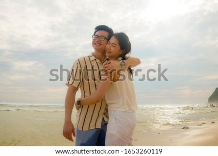 sweet and romantic lifestyle portrait of young happy Asian Chinese couple in love enjoying holiday on beautiful beach walking together by the sea playful and affectionate in relationship concept