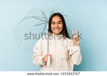 Young asian woman holding a umbrella showing number two with fingers.