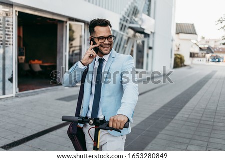 Young modern man using smart phone and driving electric scooter on city street. Modern and ecological transportation concept.