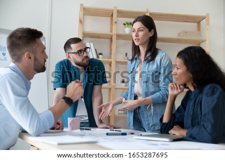 Focused young diverse employees with male team leader in glasses listening to motivated skilled female professional, sharing ideas about marketing strategy at brainstorming meeting in office. Royalty-Free Stock Photo #1653287695