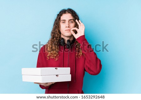 Young caucasian man holding pizzas isolated with fingers on lips keeping a secret.