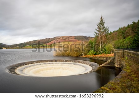 Ladybower Reservoir is the lowest of three reservoirs in the Upper Derwent . The dam's design is unusual in having two totally enclosed bellmouth overflows locally named the plugholes. Royalty-Free Stock Photo #1653296992