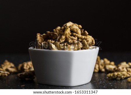 Peeled walnuts lying in a white bowl dark background warm light a healthy snack