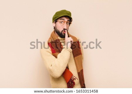 young cool bearded man asking for silence and quiet, gesturing with finger in front of mouth, saying shh or keeping a secret