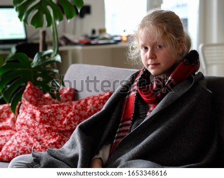 cold caucasian girl at home. portrait of a sick child in a scarf and plaid on the sofa in the apartment