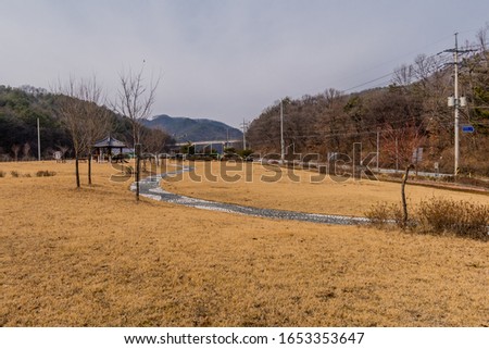 Landscape of rural public park with stone walkway leading to oriental gazebo surrounded by exercise equipment.