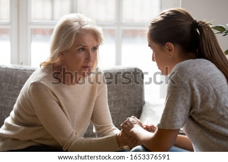 Worrying middle aged retired carrying woman sitting opposite young adult daughter, holding hands, listening to relations or health problems, showing support, giving advices, talking heart-to-heart. Royalty-Free Stock Photo #1653376591