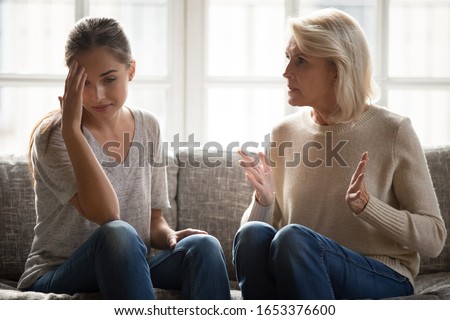Annoyed mature retired mother telling complaints, lecturing millennial grown up stubborn daughter, sitting on couch at home. Relationship problems, mutual misunderstanding, generation gap concept. Royalty-Free Stock Photo #1653376600