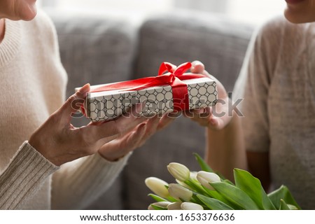 Close up image elderly womans hands holding present, receiving wrapped gift box from young daughter or grandchild. Millennial girl congratulating mature mom or granny with Mothers day or birthday.