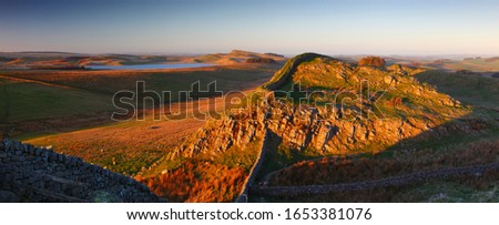 Panoramic view of Warm Evening Sunlight on Hadrians Wall and the Whin Sill, Northumberland, National Park, England, UK. Royalty-Free Stock Photo #1653381076