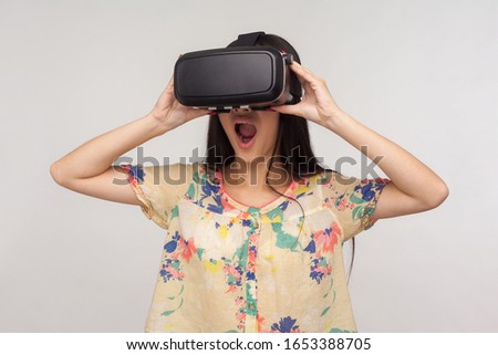 Surprised woman wearing VR glasses and watching virtual world with amazed shocked expression, playing video game, experiencing strong emotions while using simulator. indoor studio shot gray background