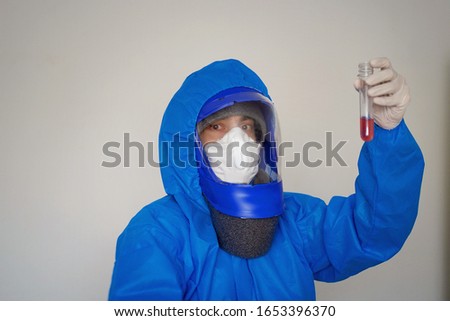 A man in a blue protective suit holds a test tube in his hands. The concept of open vaccines against coronavirus