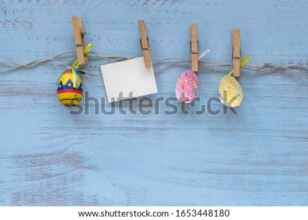 Colorful easter eggs and a blank card pinned on a rope in line on a blue wooden background. Easter holidays concept. Copyspace, place for text and wording. April vibes