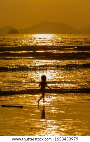Golden sand beach with wind waves surrounded by mountains and beautiful nature. With a little boy running on the beach