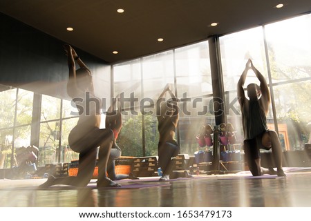 A group of young Asian people who are in good shape Doing yoga on a yoga mat With a trainer doing the example in the gym. They are in a warrior one pose. Royalty-Free Stock Photo #1653479173