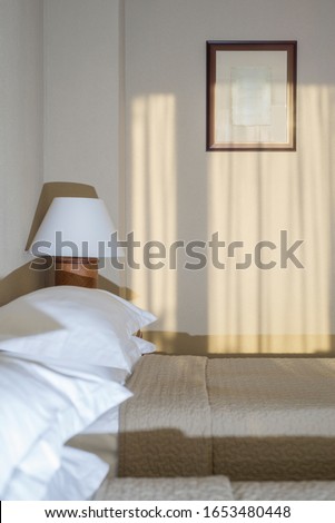 Interior details of a hotel room with a bed, bedside table, table lamp and painting.