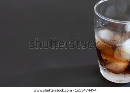 Cola drink with ice in glass on black floor.