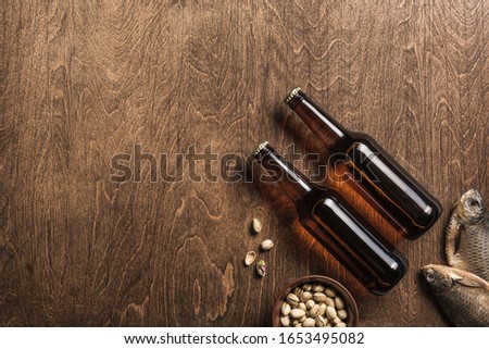 Two dark beer bottles, dried fish and a plate of pistachios on a wooden background. Top view. Copyspace. Horizontal orientation.