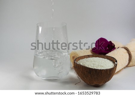 Collagen powder in half coconut. In the background, water is poured into a glass. The frame is frozen. Extra protein intake. Natural supplements for beauty and health. Collagen based plant concept. 