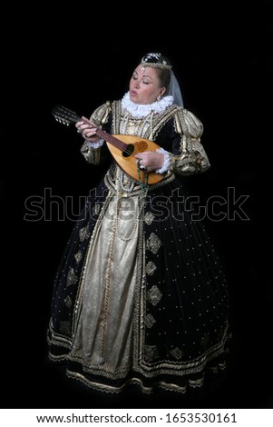 French queen Marguerite of Navarre plays mandolin on black background. Full height portrait of woman in reconstructed historical medieval royal costume of 16th century.