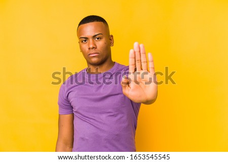 Young latin man isolated on yellow background standing with outstretched hand showing stop sign, preventing you.