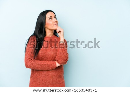 Young caucasian woman isolated on a blue background looking sideways with doubtful and skeptical expression.