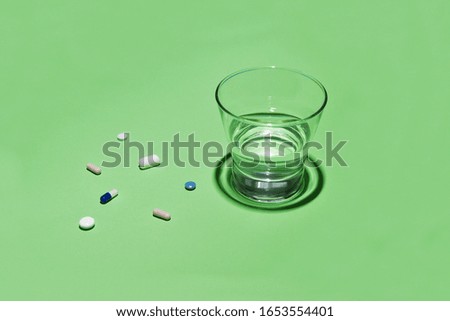 Glass of water and vitamins, pills and tablets on green background with copy space. Corona epidemic, quarantine coronavirus infection COVID-19
