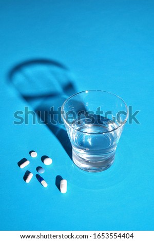 Glass of water and vitamins, pills and tablets on blue background with copy space