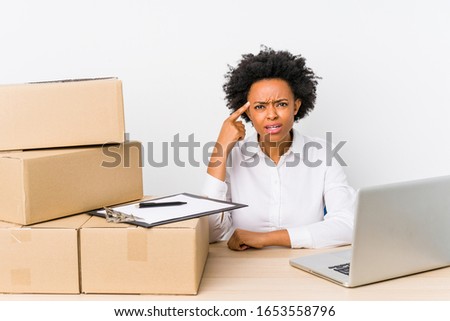 Warehouse manager sitting checking deliveries with laptop showing a disappointment gesture with forefinger.
