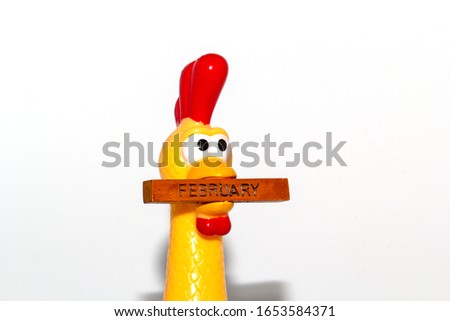 The yellow plastic chicken had a funny face, holding a piece of wood in his mouth. There were months in the wood.