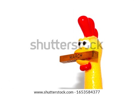 The yellow plastic chicken had a funny face, holding a piece of wood in his mouth. There were months in the wood.