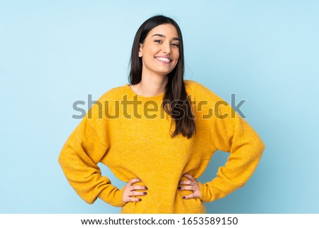 Young caucasian woman isolated on blue background posing with arms at hip and smiling