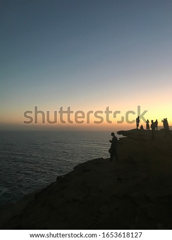 A silhouette of a group of friends at a cliff, watching the sun rise on the ocean horizon.