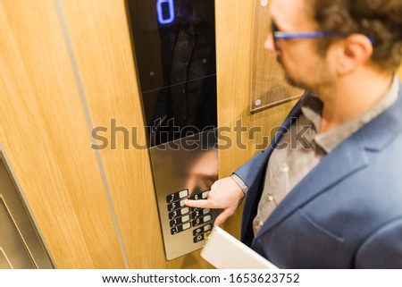 Man holding digital tablet while using elevator control panel.