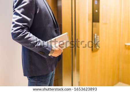 Close up of businessman with tablet device in front of modern elevator. Business and office building meeting concept.