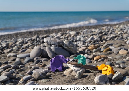Colored paper origami elephants standing on pebbles on the beach.