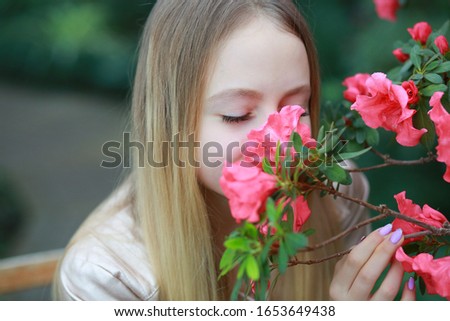 
young girl with long white hair in a jacket rests in the garden with blooming azalea