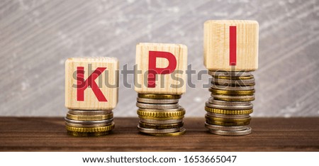 KPI (Key Performance Indicator) word written on wooden blocks on stacks of coins with grey concrete backround
